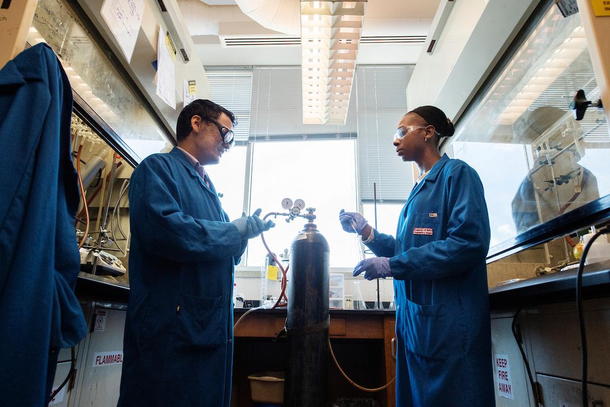 Photo of two individuals wearing lab coats in a research lab.